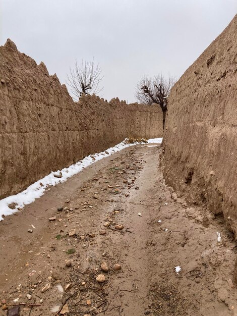 Un chemin de terre mène à travers un mur avec un sol couvert de neige.