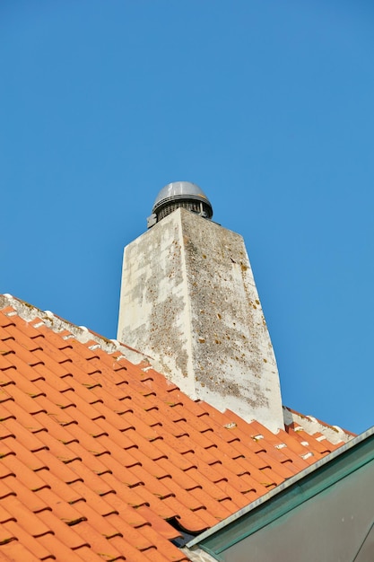 Cheminée en béton conçue sur un toit de maison en ardoise ou un bâtiment à l'extérieur sur fond de ciel bleu clair Construction d'une goulotte d'évacuation extérieure construite sur le toit pour la fumée et la chaleur du foyer