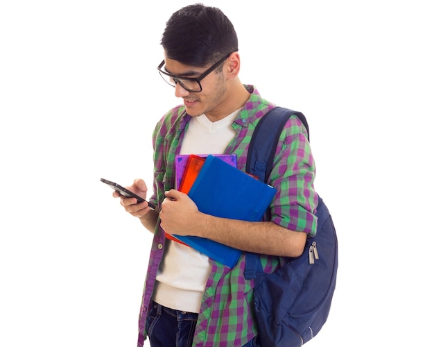 Chemise à carreaux jeune homme optimiste avec sac à dos bleu tenant des livres et utilisant un smartphone