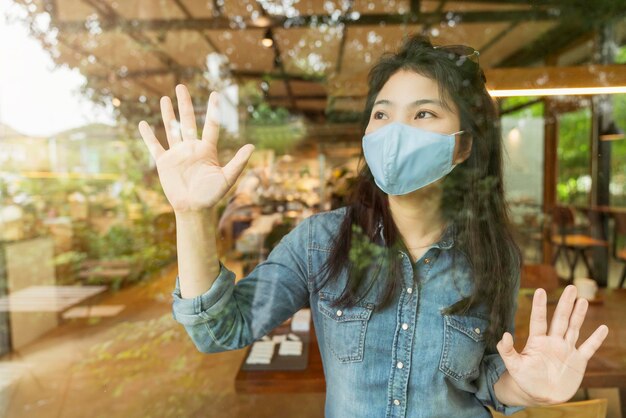 Chemise décontractée femme asiatique porter un masque facial protection contre les virus nouveau mode de vie normal s'asseoir se détendre à côté de la vitre avec reflet du jardin à l'extérieur concept de santé et d'idées