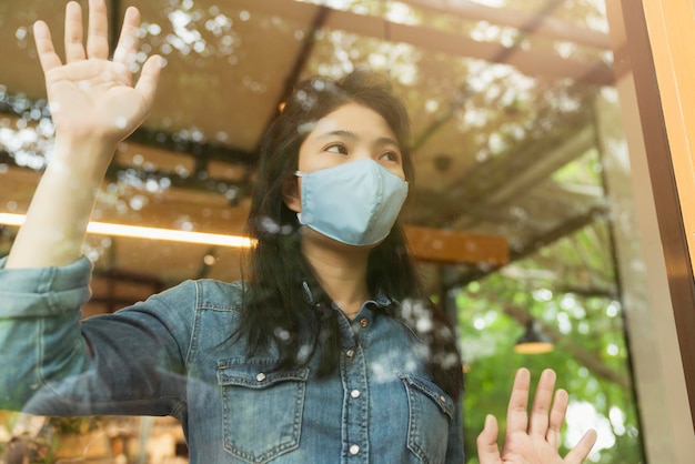 Chemise décontractée femme asiatique porter un masque facial protection contre les virus nouveau mode de vie normal s'asseoir se détendre à côté de la vitre avec reflet du jardin à l'extérieur concept de santé et d'idées