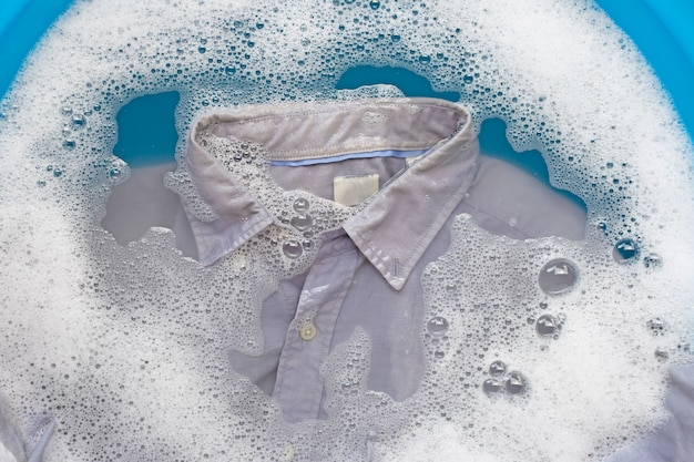 Chemise grise imbibée de détergent en poudre, dissolution de l’eau, linge à laver.