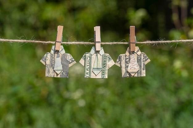 Chemise origami faite de billets de banque en dollars sur fond de nature verte suspendue Billets d'un dollar suspendus à une corde Gros plan