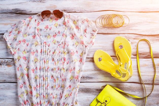 Photo chemisier col v et tongs. chaussures et bracelets jaunes pour femmes. vêtements sur plancher en bois blanc. habillez-vous pour l'été.