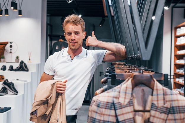 Photo cherche une veste jeune homme dans un magasin moderne avec de nouveaux vêtements vêtements élégants et chers pour hommes