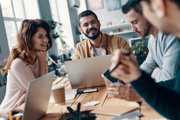 Chercher ensemble de nouvelles idées. Groupe de jeunes gens modernes en tenue décontractée élégante discutant de quelque chose et souriant tout en travaillant dans le bureau de création