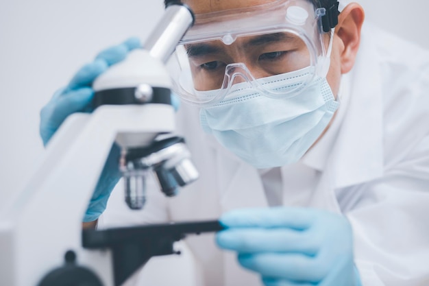 Chercheur biochimique travaillant avec un microscope pour la verrerie de laboratoire de coronavirus contenant un liquide chimique pour concevoir ou décorer la science chimie biologie médecine et concept humain