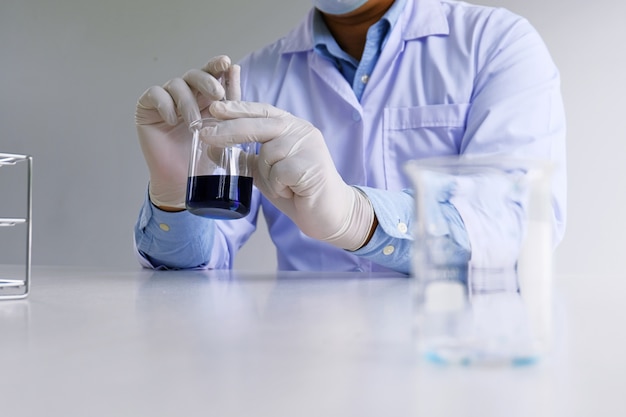 Photo le chercheur de laboratoire médical ou scientifique masculin effectue des tests avec du liquide bleu en laboratoire. concept d'équipement de laboratoire et expérimentation scientifique.