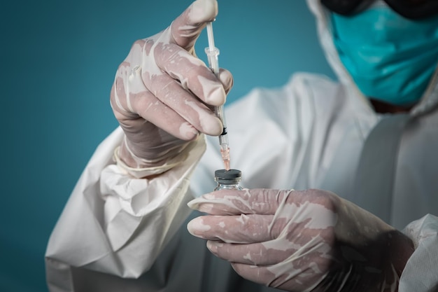 Un chercheur de laboratoire scientifique portant un masque et des gants de combinaison EPI aspire le liquide du vaccin COVID19 dans la seringue Lutte contre la pandémie de coronavirus