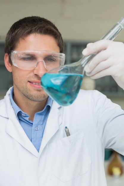 Chercheur mâle regardant la fiole avec un liquide bleu dans le laboratoire