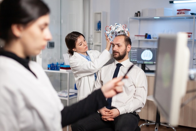 Chercheur en neurologie ajustant le casque cérébral sur le patient pendant l'étude, examinant le système nerveux. Capteurs de tomographie de haute technologie, médecin en neurosciences.