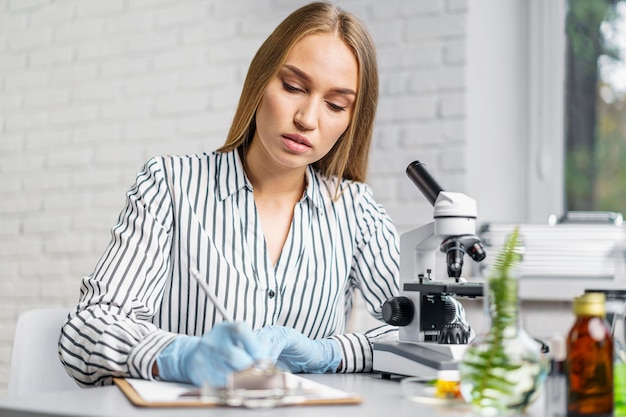 Photo chercheuse à son bureau avec microscope et presse-papiers