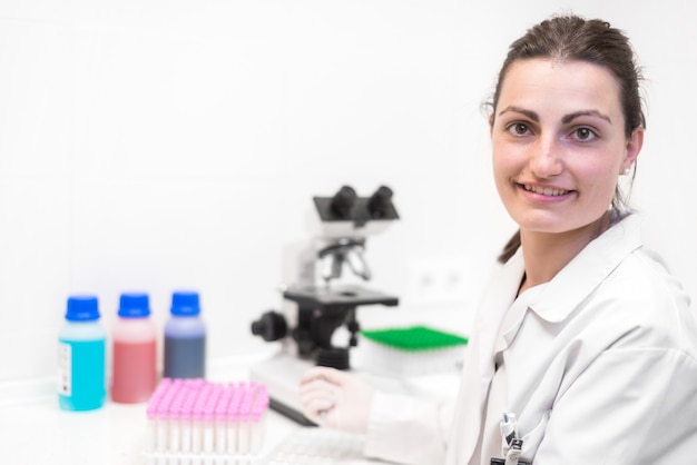 Chercheuse souriante. Chercheuse à l&#39;aide d&#39;un microscope et souriant à la caméra en laboratoire.