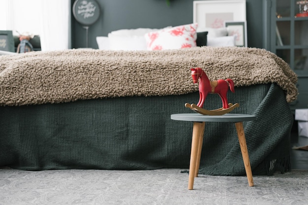 Cheval jouet en bois vintage se dresse sur un tabouret dans la chambre près du lit dans des couleurs sombres