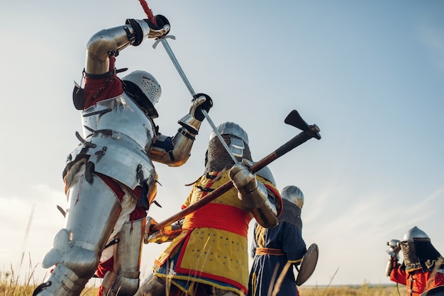 Les chevaliers médiévaux en armure et casques se battent à l'épée et à la hache, grande bataille. Ancien guerrier blindé en armure posant sur le terrain