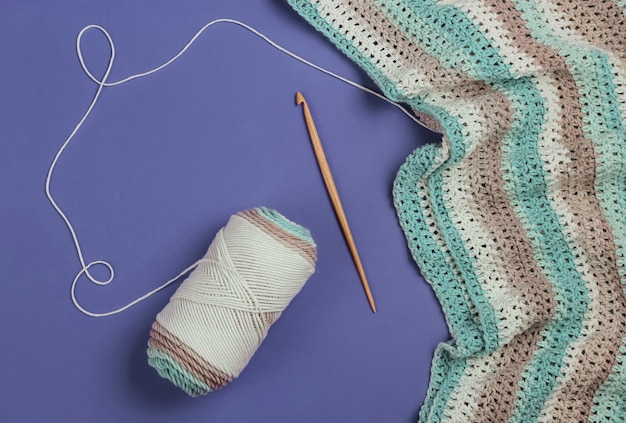 Écheveau de fils de laine avec fil et crochet en bois sur fond violet. Passe-temps