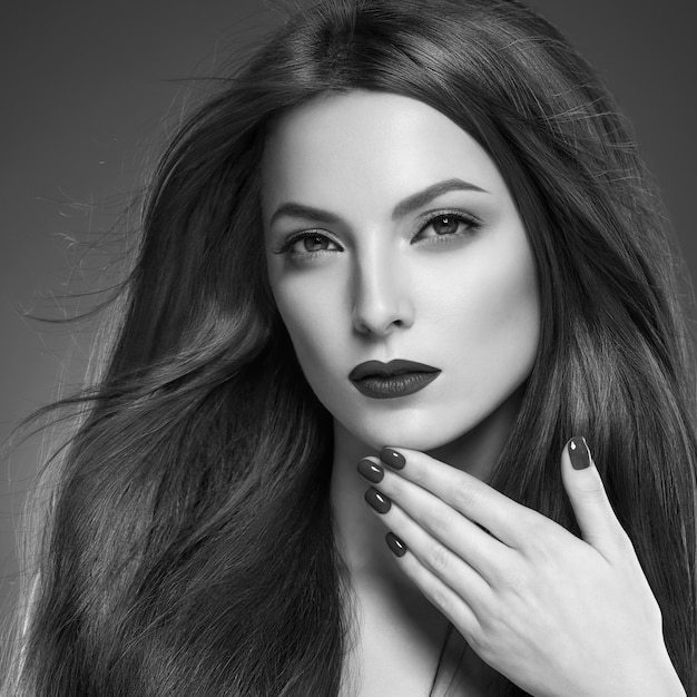 Cheveux beauté femme longue bruette lisse belle manucure ongles modèle rouge à lèvres fond brun maquillage de soirée portrait. Prise de vue en studio. Gris. Monochromes. Noir et blanc.