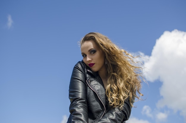 Cheveux blonds bouclés femme extérieur fond de ciel avec veste en cuir