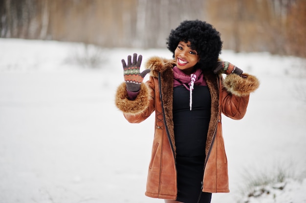 Les cheveux bouclés femme afro-américaine portent sur le manteau et les gants en peau de mouton posés au jour d'hiver, montrent cinq doigts.