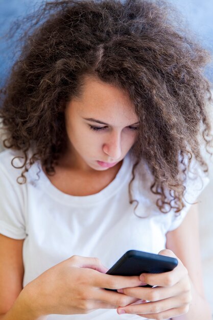 Cheveux frisés teen girg messaning sur le téléphone mobile