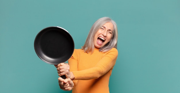 Cheveux gris jolie femme d'âge moyen apprentissage cuisinier avec une casserole