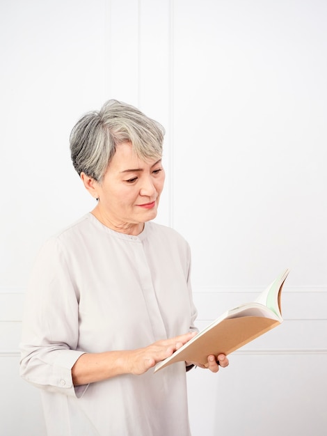 Cheveux gris senior femme asiatique tenant et lisant un livre à la maison.