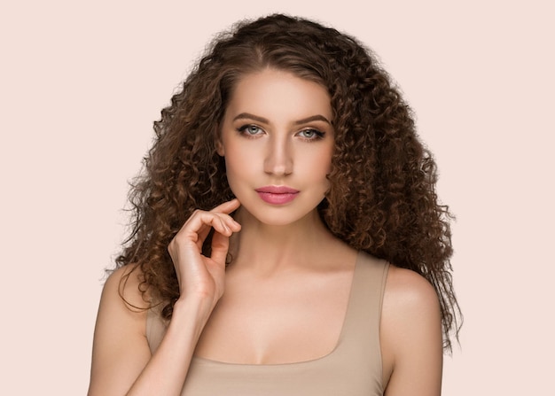 Cheveux longs bouclés brune jeune femme touchant le portrait féminin de la beauté du visage. Couleur de fond rose