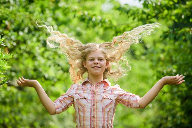 Cheveux longs et sains petite fille heureuse avec de longs cheveux sains santé et soins des cheveux coiffeur mode longs cheveux blonds bouclés petite fille dans la forêt verte vacances d'été journée des enfants