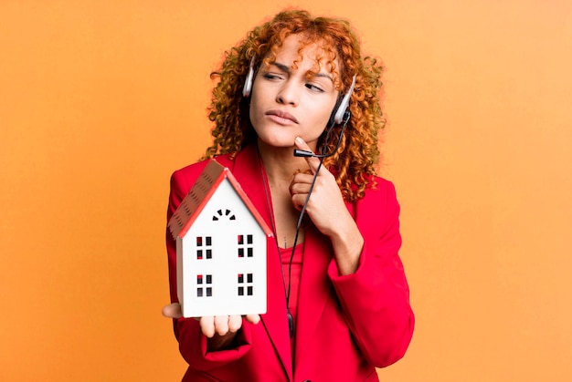 Photo cheveux roux jolie femme agent immobilier avec un modèle de maison et un casque