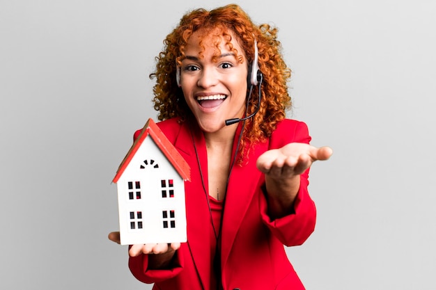 Cheveux roux jolie femme agent immobilier avec un modèle de maison et un casque