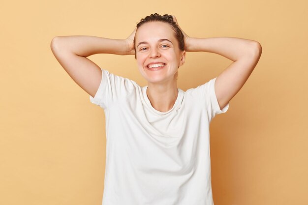 Cheveux sains Lavage de bien-être Routine de bien-être Une femme souriante satisfaite portant un T-shirt blanc lave les cheveux debout avec de la mousse de shampoing sur sa tête isolée sur fond beige