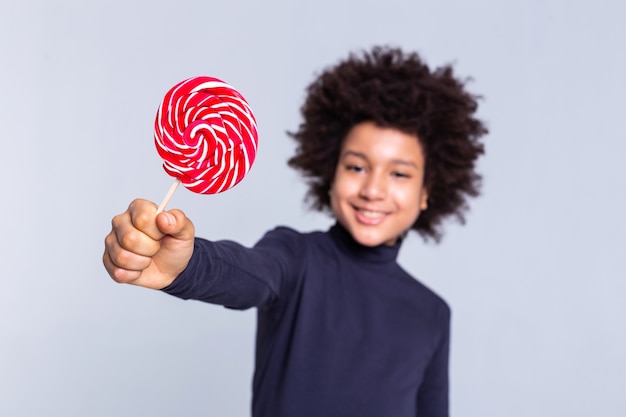 Les cheveux sauvages. Garçon joyeux aux cheveux noirs résolu tirant la main avec des bonbons dedans et l'air extrêmement fier