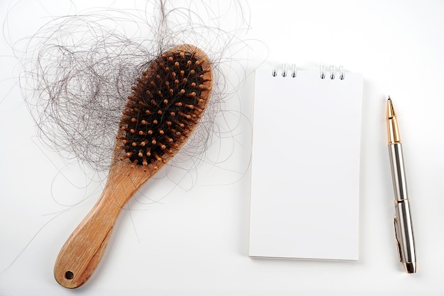 Les cheveux tombent dans le peigne avec un cahier et un stylo les cheveux tombent tous les jours de sérieux problèmes sur fond blanc