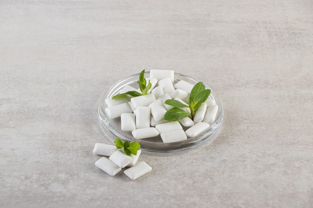 Chewing-gums blancs avec des feuilles de menthe placés sur une table en pierre.