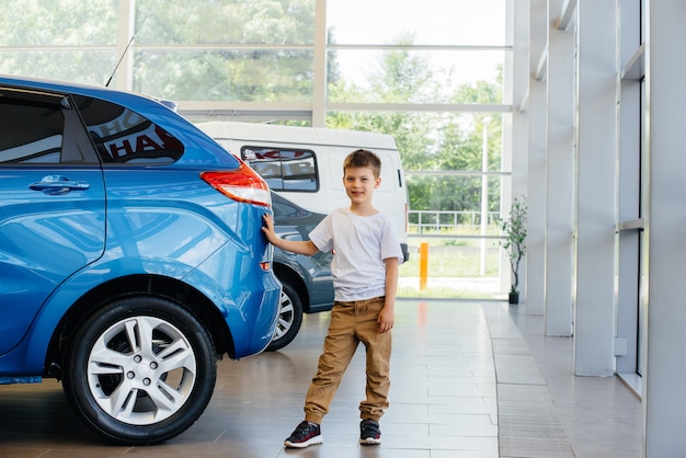 Chez un concessionnaire automobile, un garçon heureux se tient près d'une nouvelle voiture avant de l'acheter. Achat de voiture.