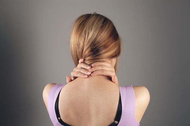 Chez une jeune femme, l'arrière de la tête fait mal sur fond gris