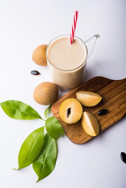 Chickoo, Chikoo OU Sapota Milkshake savoureux et sain. C'est un fruit sain mélangé avec du lait et de la glace servi dans un verre sur fond coloré ou en bois. Mise au point sélective