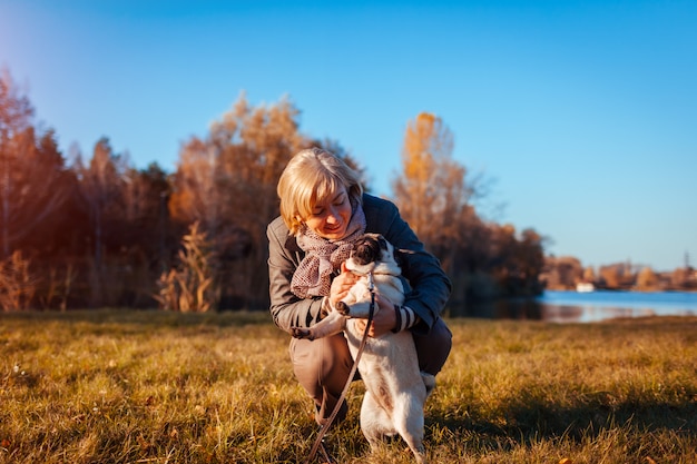 Chien Carlin en automne parc par la rivière. Heureuse femme étreignant son animal de compagnie et s'amuser avec sa meilleure amie.