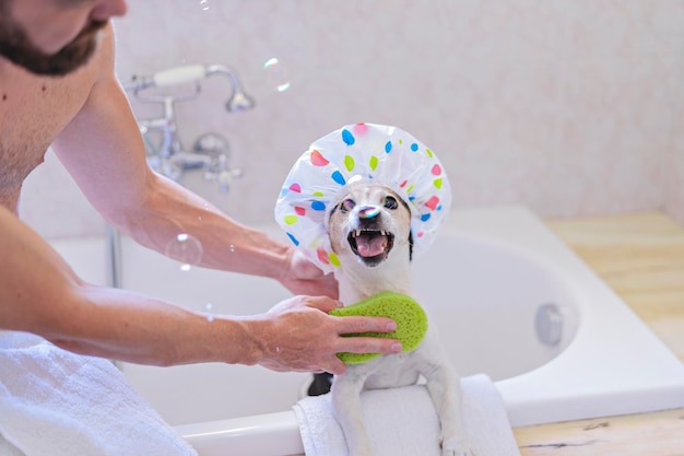 Chien drôle avec bonnet de douche s'amusant avec des bulles de savon dans la salle de bain avec le propriétaire