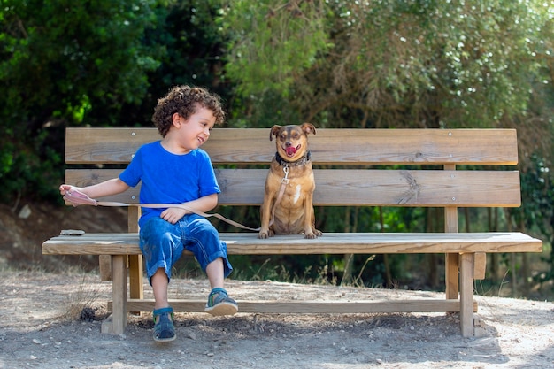 Chien et enfant assis sur un banc en bois dans le parc. l'enfant regarde son chien et rit par une journée ensoleillée