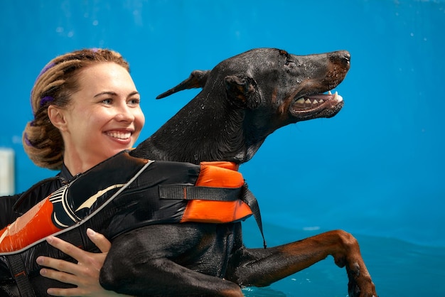 Chien en gilet de sauvetage nage dans la piscine avec entraîneur entraînement à la réadaptation des animaux de compagnie