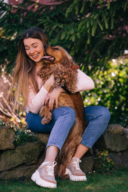 Chien heureux léchant le visage d'une femme assise sur la cour près de tre