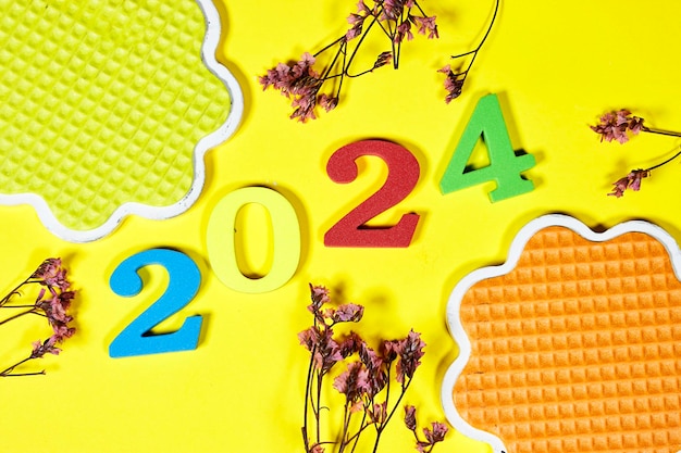 Chiffres d'éponge colorés du numéro du Nouvel An 2024 et soucoupe en forme de design avec gypsophile rose sur jaune