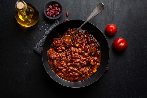 Chili con carne cuit servi dans un bol prêt à manger sur fond sombre.