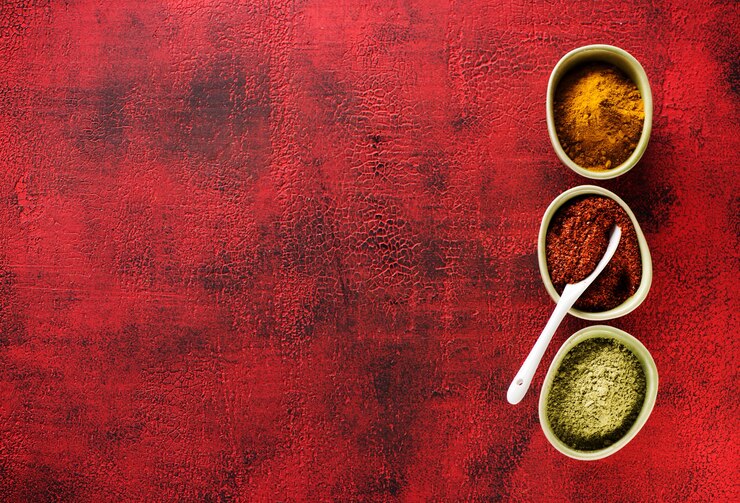 Chili en poudre, curry de curcuma et cardamome. Assaisonnement aux épices indiennes épicées dans des bols sur fond rouge et espace de copie, vue de dessus.