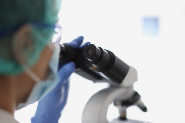 Chimiste de femme dans le gant protecteur bleu regarde le microscope dans le laboratoire de chimie