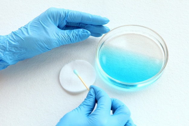 Chimiste à lueurs bleues au laboratoire testant le liquide bleu de la plaque de verre et l'échantillonneur sur ses mains