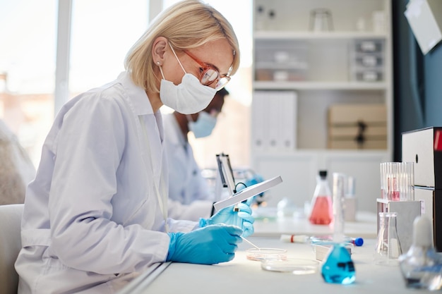 Une chimiste qui regarde à travers une loupe dans une plaque de Pétri en train d'étudier des cellules en laboratoire