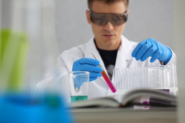 Un chimiste de sexe masculin tient un tube à essai de verre dans sa main déborde d'une solution liquide