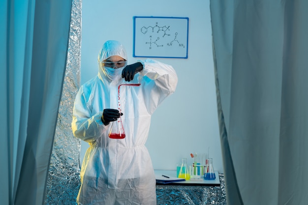 Un chimiste en tenue de protection et des gants travaillant avec des flacons en verre.